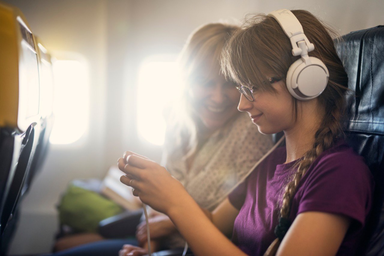 Mother and daughter travelling by plane. They are sitting comfortably and smiling happily. Daughter is using the smartphone and mother is also looking at her phone.
